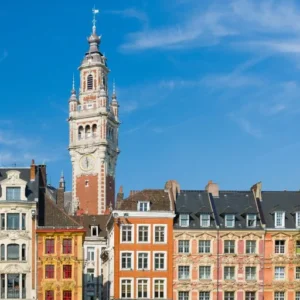 Beffroi de l'hôtel de ville de Lille qui dépasse d'une rangée d'immeubles à 3 étages. Avec un ciel bleu, légèrement nuageux.